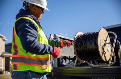 Employee in vest and hardhead holding fiberoptic cable.