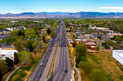 Road in Fort Collins with buildings on either side and foothills in the background.